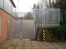 2400mm high galvanised steel palisade fencing and access gate. Pales are closed spaced to prevent access to the emergency gate release lock. A small quadrant has been secured where the fence steps in height.